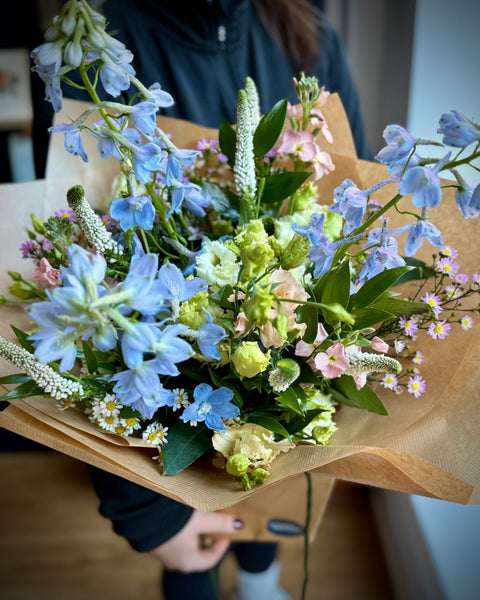 Bouquet of flowers wrapped in brown paper held by a person.