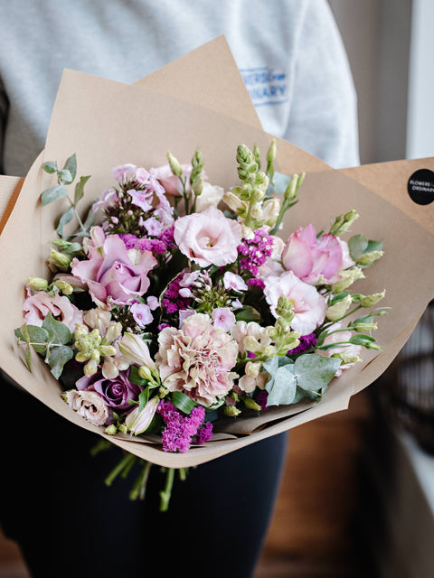 Bouquet of pink flowers wrapped in brown paper held by a person.