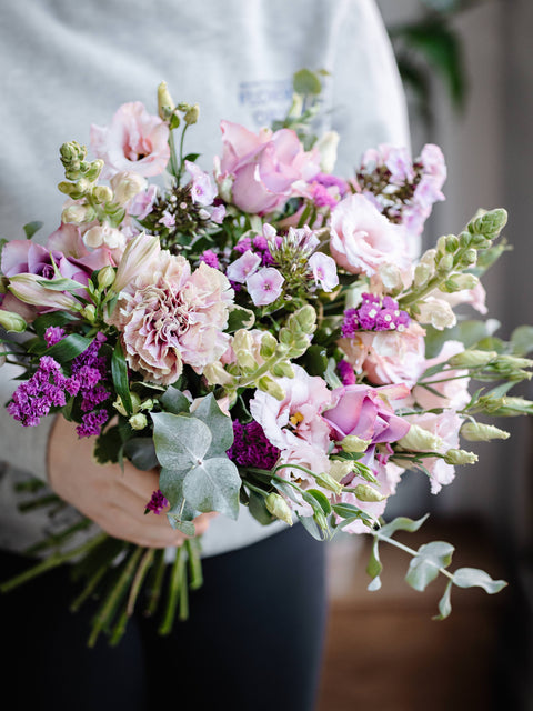 Bouquet of pink and purple flowers held by a person with a blurred background