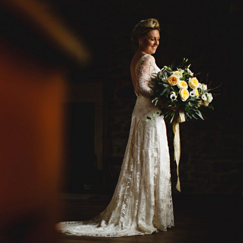 Bride in a lace wedding dress holding a bouquet of flowers against a dark background
